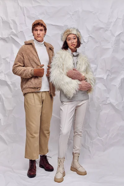 Interracial fashion models in cold-weather clothes looking at camera on white textured backdrop — Stock Photo