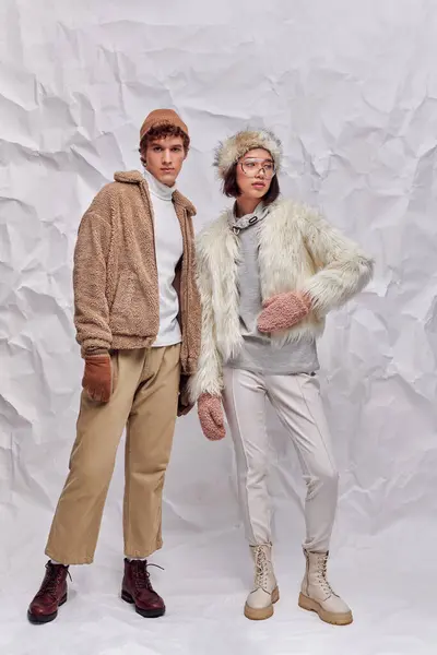 Полная длина межрасовой пары в уютном зимнем наряде на белом текстурированном фоне, зимняя мода — стоковое фото