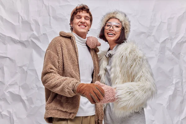 Trendy multiethnic couple in stylish winter clothes smiling at camera on white textured backdrop — Stock Photo