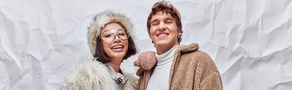Happy interracial couple in stylish winter wear looking at camera on white textured backdrop, banner — Stock Photo