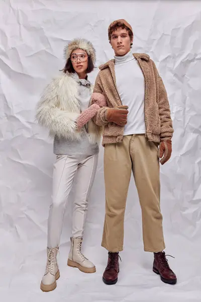 Young interracial couple in cold-weather attire standing on white textured backdrop, winter styling — Stock Photo