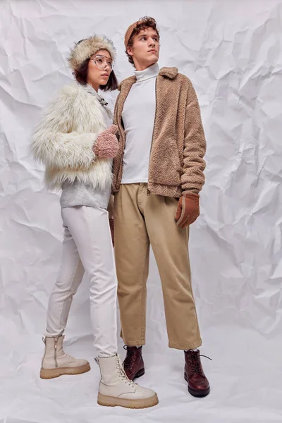 Couple interracial dans des tenues d'hiver élégantes regardant loin sur fond blanc texturé, tendance saisonnière — Photo de stock