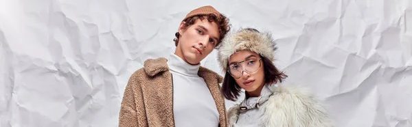 Style d'hiver, couple interracial en fausse fourrure vestes et chapeaux sur fond texturé blanc, bannière — Photo de stock