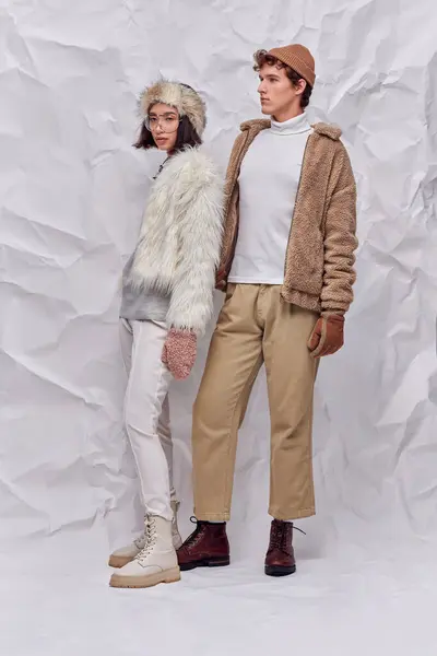 In voller Länge trendige interrassische Models in winterlichen Outfits vor weiß strukturiertem Hintergrund, moderner Trend — Stockfoto