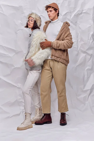 Full length of multiethnic couple in worm cozy outfits looking away  on white textured backdrop — Stock Photo