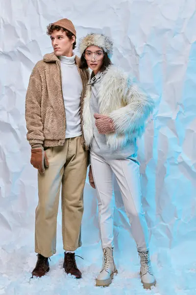 Interracial couple in faux fur jackets and boots on white textured backdrop, winter fashion shoot — Stock Photo