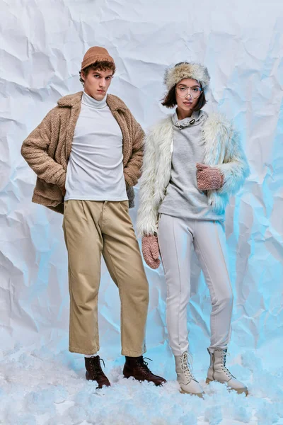 Wintermode-Lookbook, gemischtes Paar in warmer Freizeitkleidung posiert auf weißem Schnee im Atelier — Stockfoto
