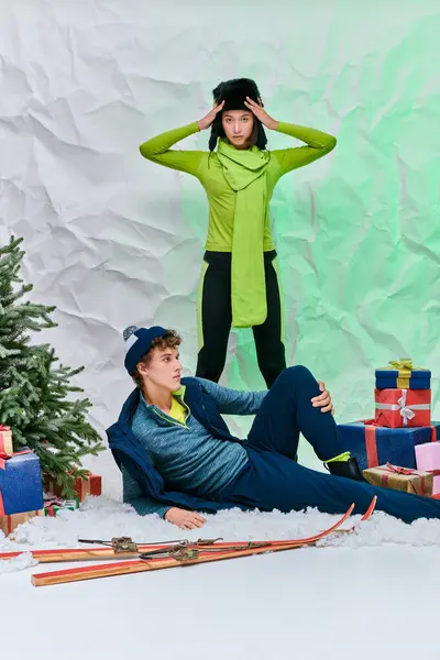 Élégant modèle asiatique regardant caméra près de l'homme sur la neige près de boîtes-cadeaux et arbre de Noël en studio — Photo de stock