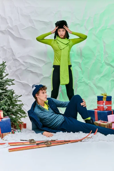 Stylish asian model looking at camera near man on snow near gift boxes and christmas tree in studio — Stock Photo