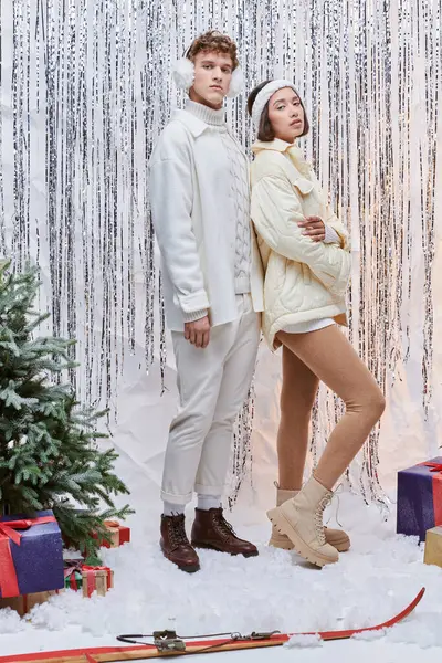 Modelos interracial posando cerca de oropel de plata, cajas de regalo y árbol de Navidad en estudio festivo - foto de stock