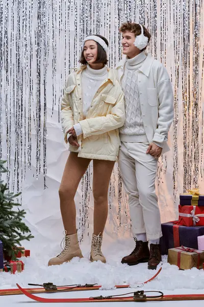 Couple multiethnique en vêtements d'hiver près de présent et arbre de Noël sur fond de mousseline brillant — Photo de stock