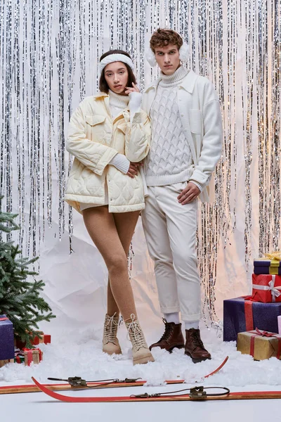 Trendy interracial models looking at camera near christmas tree and presents on shiny backdrop — Stock Photo
