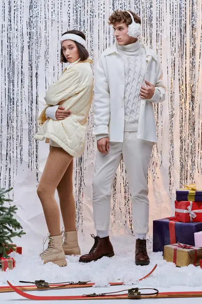 Élégant couple multiethnique debout près de l'arbre de Noël et présente sur fond de tinsel brillant — Photo de stock