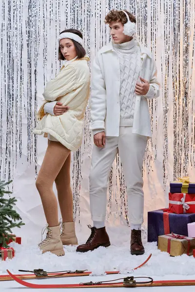 Stylish multiethnic couple standing near christmas tree and presents on shiny tinsel backdrop — Stock Photo