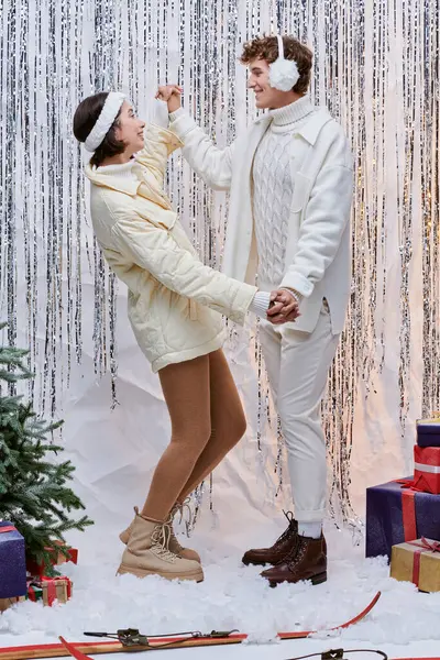 Joyful interracial couple holding hands near christmas tree, gift boxes and silver tinsel in studio — Stock Photo