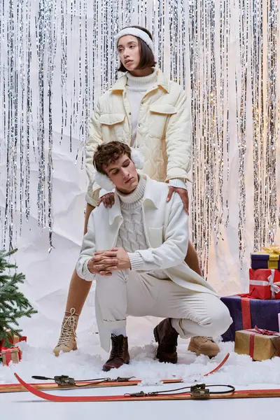 Modelos multiétnicos en moda ropa de invierno posando cerca del árbol de Navidad, cajas de regalo y oropel de plata - foto de stock