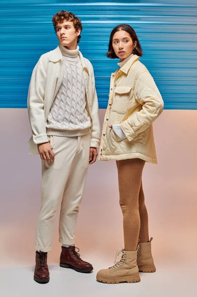 Modelos multiétnicos em jaquetas quentes e botas de couro perto de folha de plástico azul, moda de inverno — Fotografia de Stock