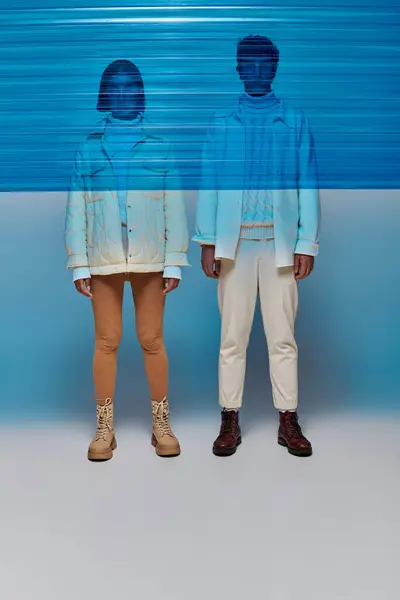 Міжрасові пари в куртках і шкіряних чоботях, що стоять за синьою пластиковою панеллю, зимовий стиль — стокове фото
