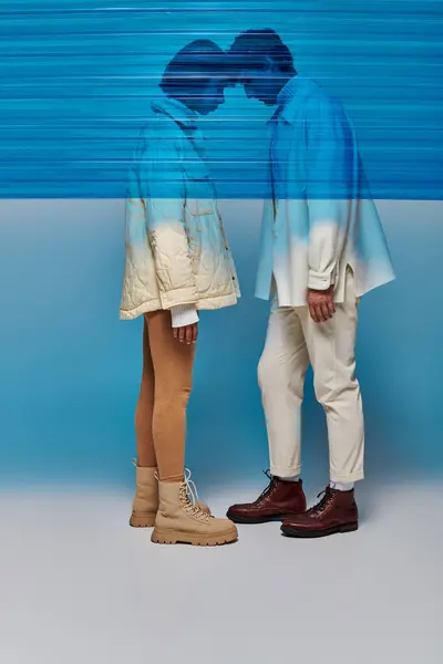 Вид сбоку на мультиэтнические модели в зимнем наряде, позирующем голова к голове за синей пластиковой панелью — стоковое фото