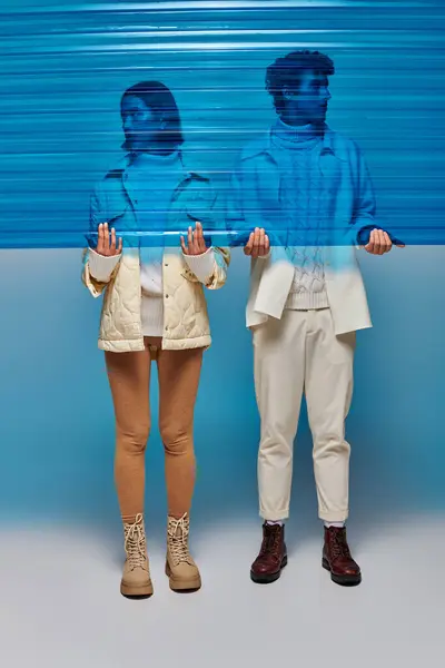 Jovem casal interracial em botas de couro segurando folha de plástico azul em estúdio, conceito de estilo de inverno — Fotografia de Stock