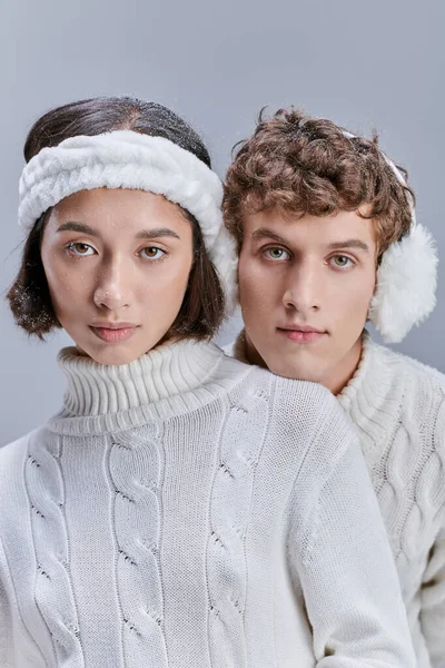 Jeunes modèles interracial en vêtements chauds et confortables regardant la caméra sur gris, campagne de mode d'hiver — Photo de stock