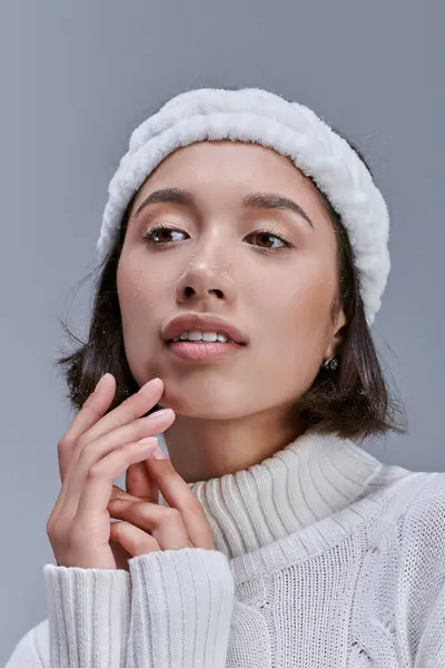 Romantique et rêveuse asiatique femme en hiver pull et tiède blanc bandeau regardant loin sur gris — Photo de stock