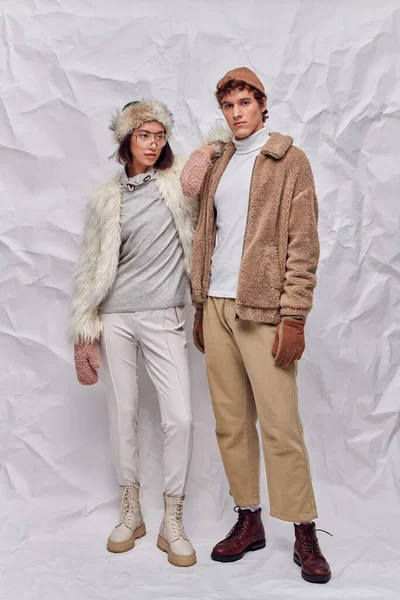 Longitud completa de la pareja interracial en traje caliente de pie sobre fondo de textura blanca, estilo de invierno - foto de stock