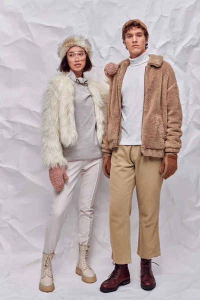 Full length of multiethnic couple in cozy clothes posing on white textured backdrop, winter fashion — Stock Photo