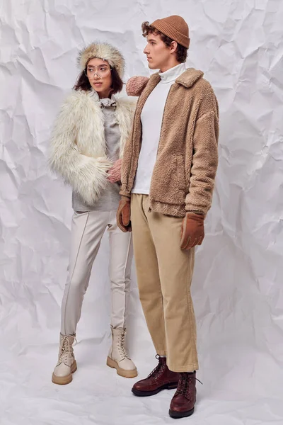 Fashionably dressed interracial couple looking away on white textured backdrop, stylish winter — Stock Photo