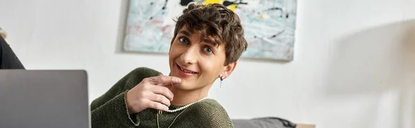Happy and curly transgender blogger using laptop in bedroom at home, social media influencer banner — Stock Photo