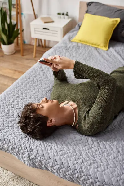 Transgender blogger with curly hair using smartphone and lying on bed, social media influencer — Stock Photo