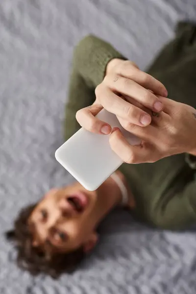 Focus sur smartphone, blogueur transgenre couché sur le lit et utilisant le téléphone, influenceur des médias sociaux — Photo de stock