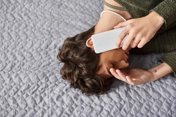 Triste persona transgénero rizado en traje casual hablando en el teléfono inteligente en el dormitorio, llamada telefónica — Stock Photo