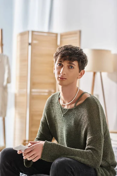 Young transgender person in casual attire looking at camera and sitting in modern apartment — Stock Photo