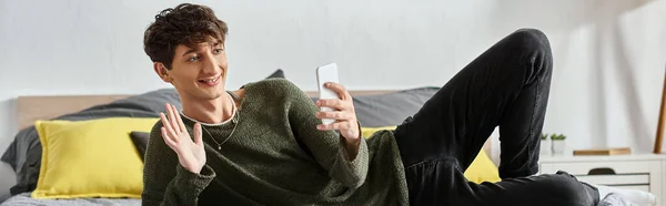 Happy and curly transgender social media influencer waving hand during online streaming, banner — Stock Photo