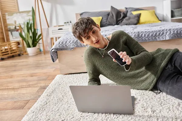 Happy transgender influencer using laptop and holding smartphone while sitting on carpet, blogger — Stock Photo