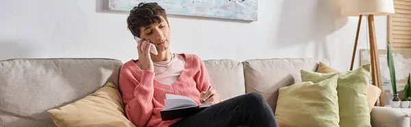 Transgender blogger in pink sweater talking on smartphone and writing in notebook, banner — Stock Photo