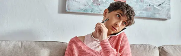 Transgender blogger in pink sweater talking on smartphone and holding pen, horizontal banner — Stock Photo
