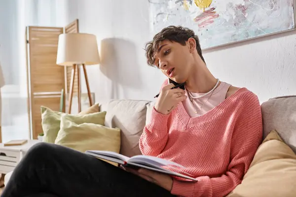 Transgender freelancer in pink sweater talking on smartphone and writing in notebook at home — Stock Photo