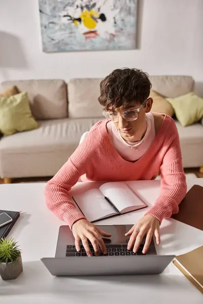 Young androgynous freelancer in pink sweater and eyeglasses typing on laptop while working remotely — Stock Photo