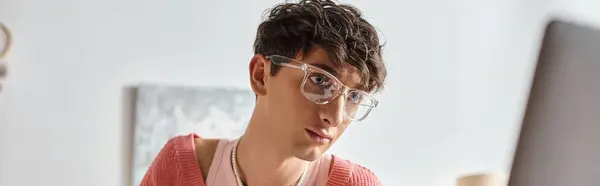 Curly androgynous freelancer in pink sweater and eyeglasses looking at laptop, horizontal banner — Stock Photo