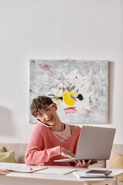 Cheerful androgynous freelancer in pink sweater and eyeglasses using laptop and smartphone at home — Stock Photo