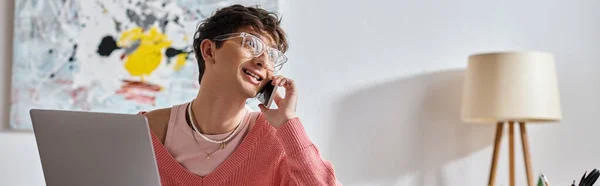 Cheerful androgynous freelancer in pink sweater and eyeglasses using laptop and smartphone, banner — Stock Photo