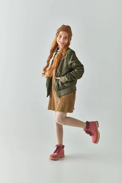 Kindermode, fröhliches Mädchen mit langen Haaren und Wintermütze auf dem Kopf in Kleid und Jacke — Stockfoto