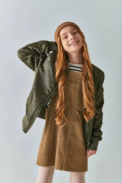 Moda infantil, chica alegre con pelo largo y sombrero de punto de pie en vestido y chaqueta de invierno - foto de stock