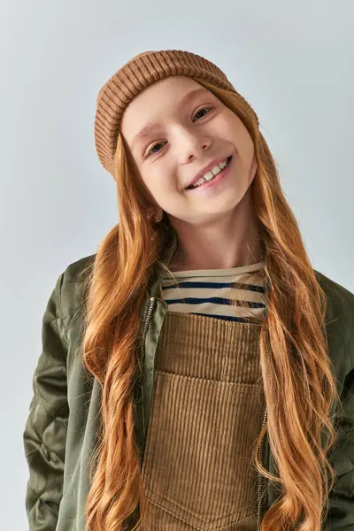 Moda de inverno, menina alegre em chapéu de malha e outerwear olhando para a câmera no fundo cinza — Fotografia de Stock