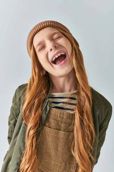 Mode d'hiver, fille étonnée en tricot chapeau et vêtements de plein air posant avec bouche ouverte sur fond gris — Photo de stock