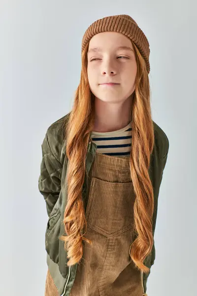 Skeptical preteen girl  with long hair posing in winter outfit and knitted hat on grey backdrop — Stock Photo