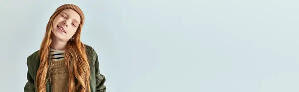 Cute girl in knitted hat grimacing and looking at camera on grey backdrop, winter fashion banner — Stock Photo