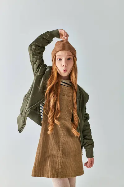 Menina pré-adolescente em roupa de inverno elegante tocando chapéu de malha e lábios bebendo em pano de fundo cinza — Fotografia de Stock
